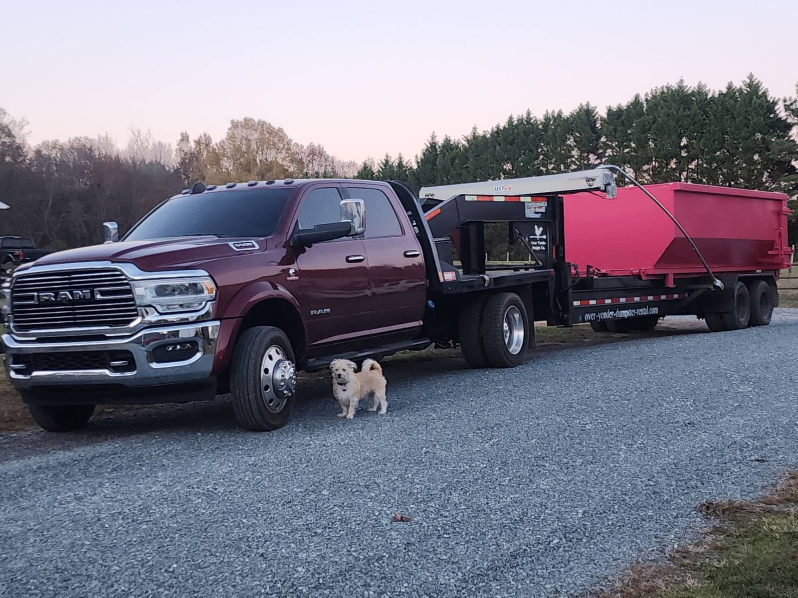 Burgundy Ram dumpster truck with red roll-off dumpster on a gravel driveway in North Carolina